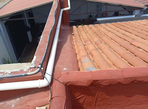 Caño de PVC blanco tendido sobre una medianera, junto a un techo de tejas
